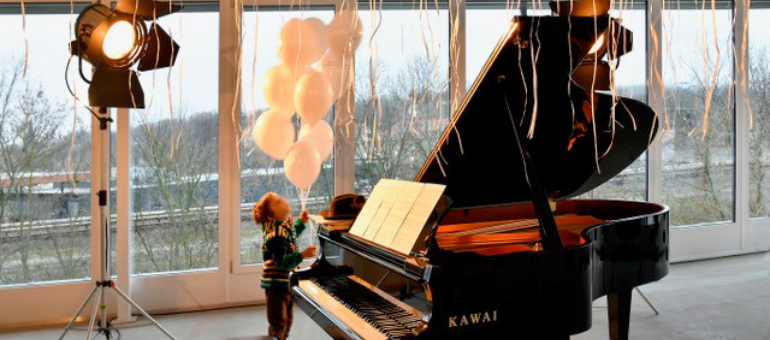 Kind steht neben einem Klavier und hält weiße Luftballons in der Hand