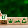 Eine Hand dreht einen Würfel um, auf welchem 2024 und 2024 steht. Daneben sind weitere Würfel, die Symbolbilder zum Thema Nachhaltigkeit enthalten.