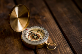 Ein goldener, aufgeklappter Kompass auf dunklem Holztisch liegend